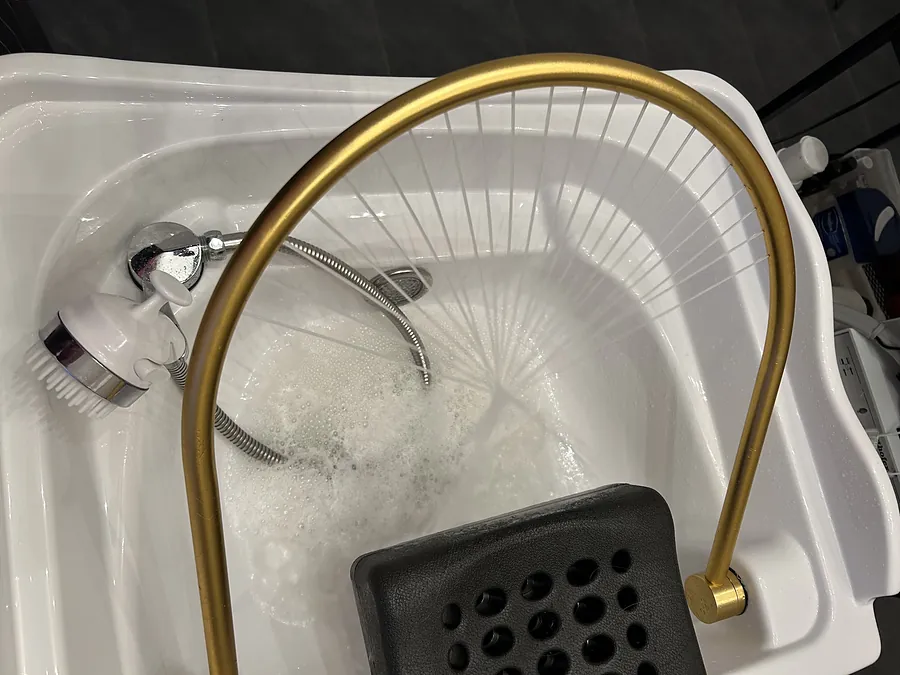 Het head spa bad in de salon: wit bekken met een gouden boog waar het water uit valt